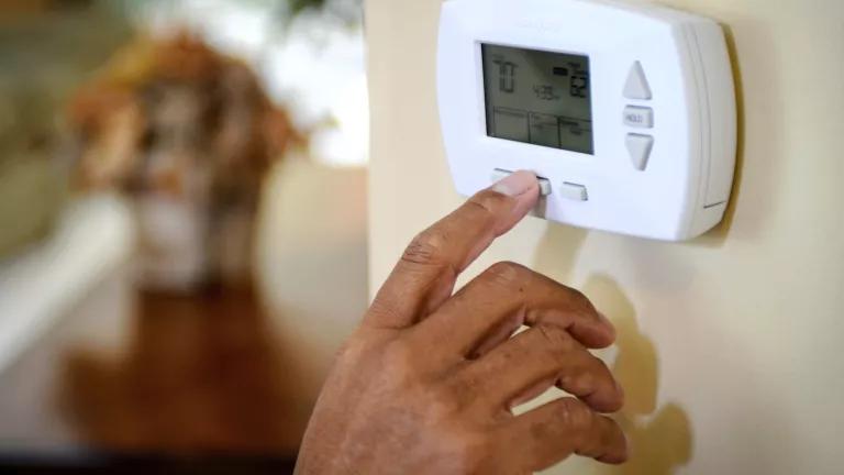 A person adjusting a digital thermostat control in their home.