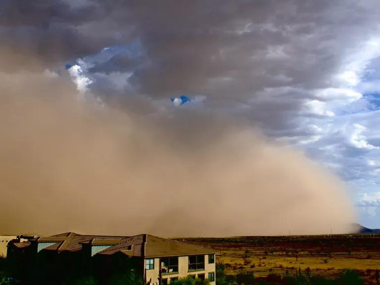 A row of homes sit in the foreground with a huge cloud of dust overtaking the horizon