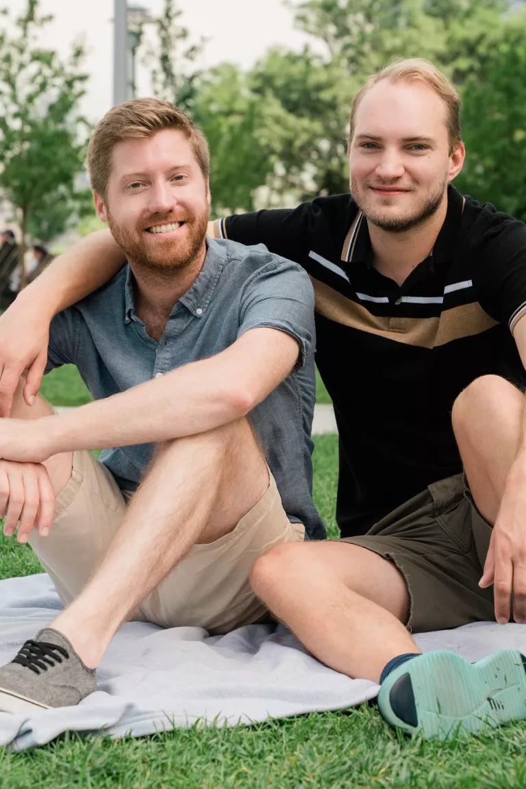 A smiling couple sitting on a picnic blanket on grass at Domino Park, Brooklyn