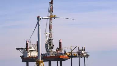 An offshore wind turbine blade is placed into the nacelle during construction of an offshore wind turbine.