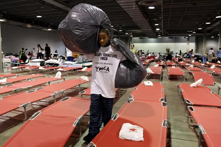 A boy carries two filled garbage bags are he walks past rows of cots