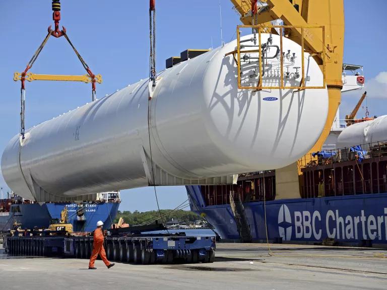 A large white tank suspends from a crane