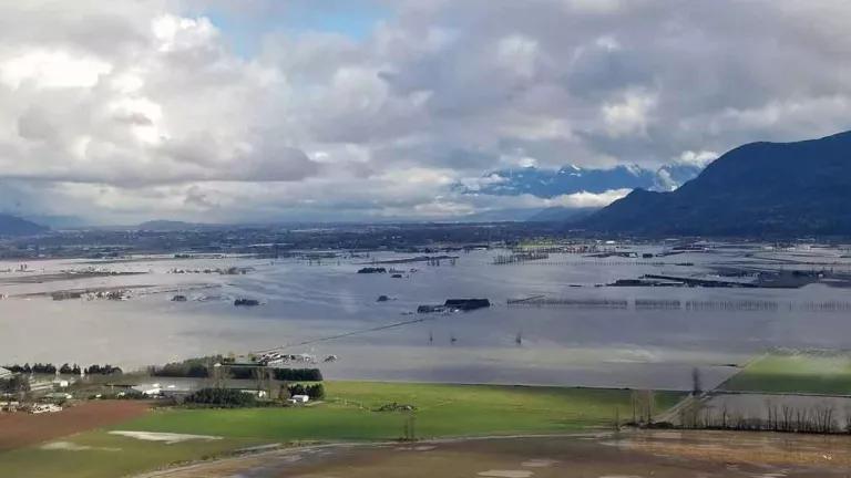 A flooded valley with homes and green fields and a mountain in the background