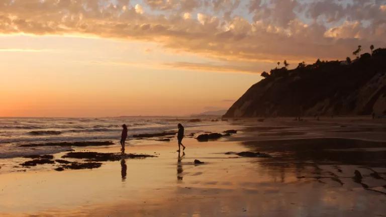 Two people walk along a beach as the sun sets