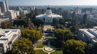 Aerial view of trees, and a landscaped roundabout leading up to the California State Capitol building