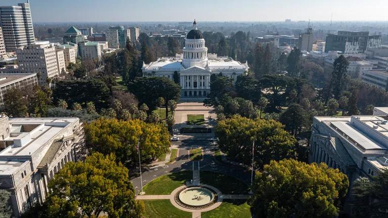 Aerial view of trees, and a landscaped roundabout leading up to the California State Capitol building