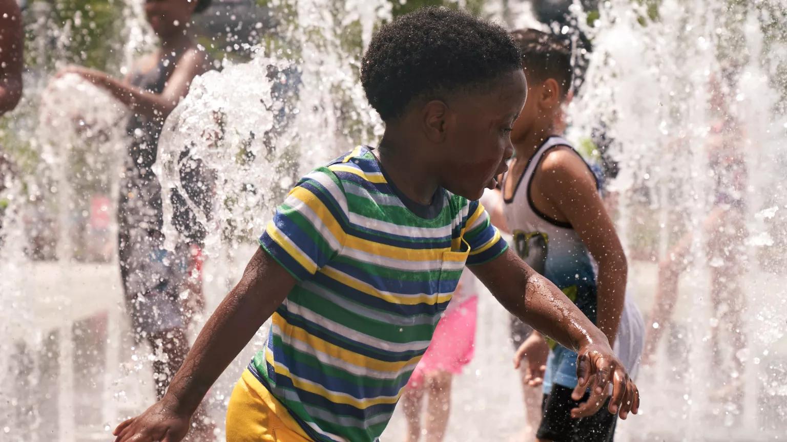 Two young children playing in sprinklers in a city park