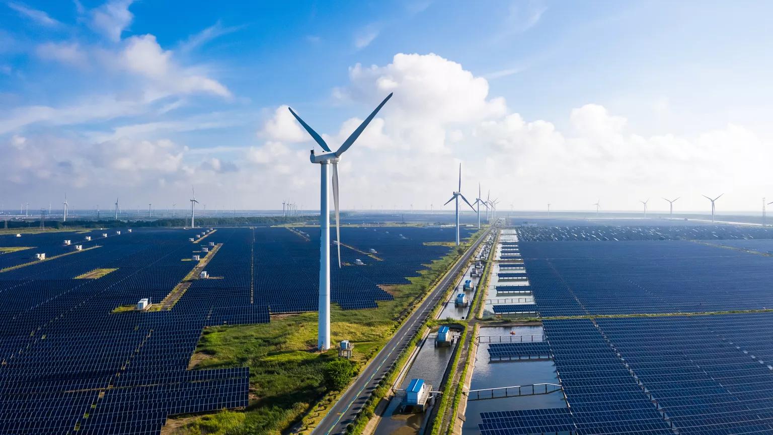 An aerial view of solar arrays and wind turbines at a power station against a blue sky in Yancheng City, China