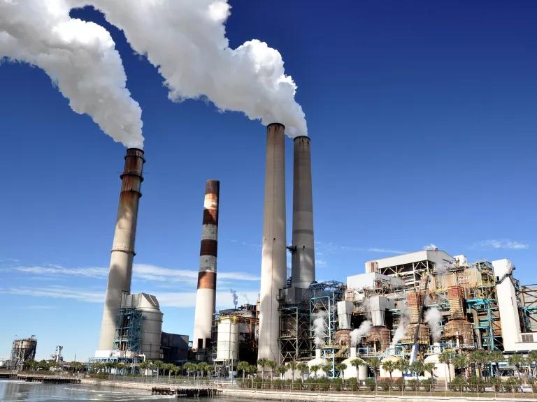 Smoke blows out of three tall smokes stacks at a power plant, with blue sky in the background