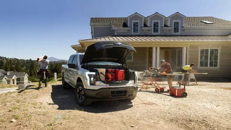 An electric pickup truck with its front trunk open is parked in front of a home that is under construction