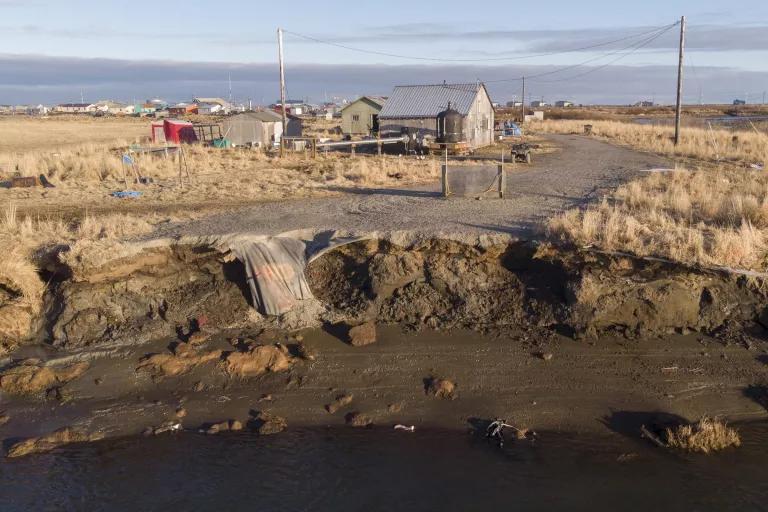 An eroded bank of land down the road from a house in the background