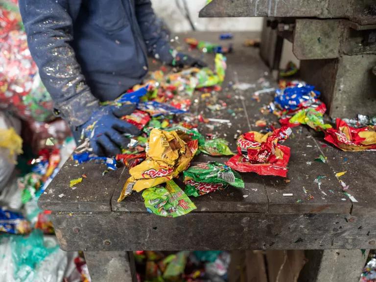 A person stands at a workbench covered in shredded plastic chips bags.