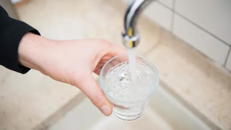 A person filling a glass of water from a sink faucet.