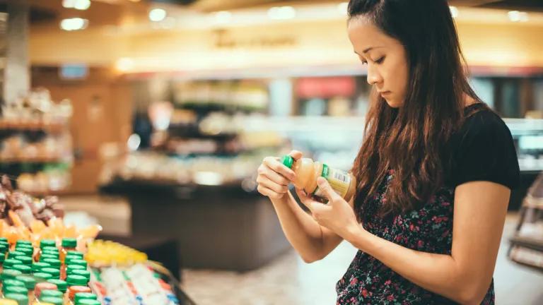 A woman reading a bottled juice drink label as she shops for groceries.