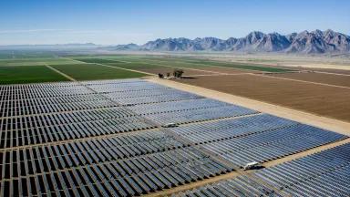 A field of solar panels with green grass and mountains in the background