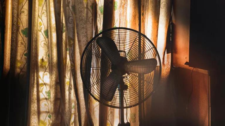 A floor fan in a dark room, placed in front of a window with the curtains closed