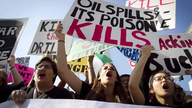 Young people carry protest signs that read "kill the drill" and "oil spills its poison."