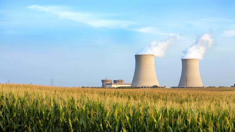 Two large nuclear cooling towers stand in the distance with a cornfield in the foreground