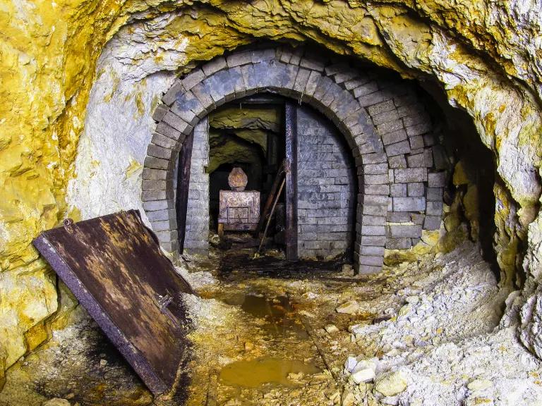 A tunnel is formed out of rock, with a brick doorway and facade at the far end. The rock surfaces are covered in a yellow-brown subtance.