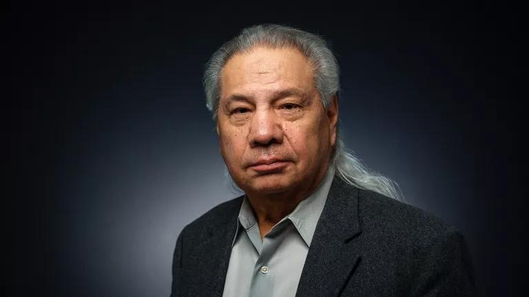 Portrait of John Echohawk looking directly at camera in a studio against a dark background