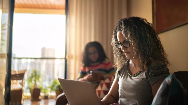 A woman sits on a couch working on a laptop