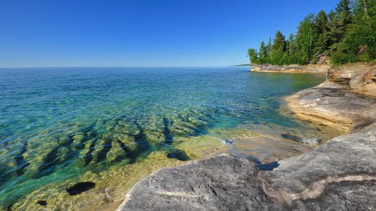 Large, smooth rocks on the shoreline of a clear, blueish green lake