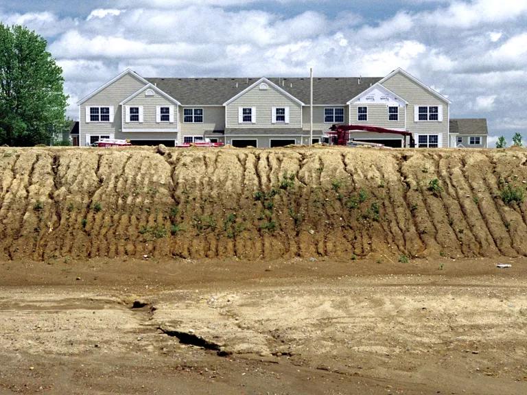 A house sits atop a dried-out ledge, with vertical crevices visible in the dirt