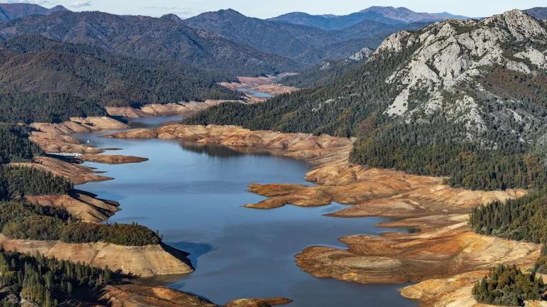 A river runs through a valley between mountains, with brown banks visible on either side of the water