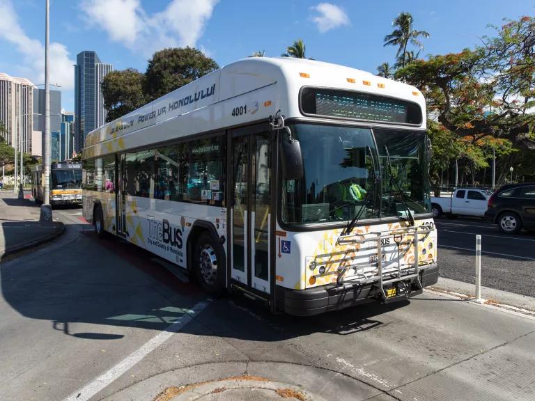 A bus drives down a city street with high rise buildings in the background