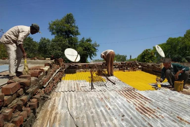 Three men stand on a flat metal roof painting it yellow