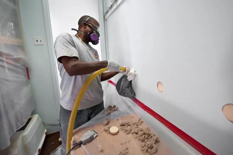 A worker with a facemask on sprays insulation into a wall