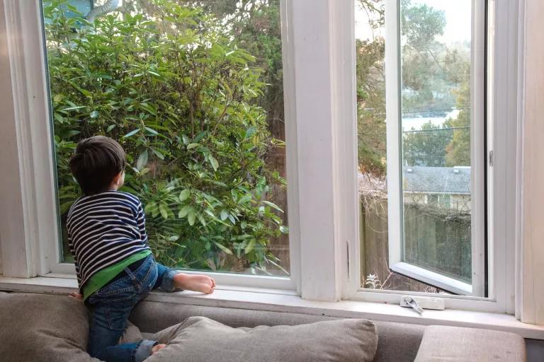 A young child sits on the sill of a large window