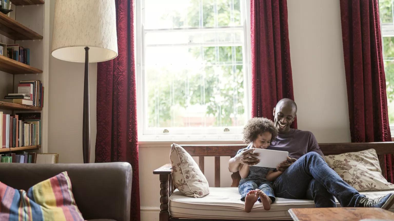 A man and small child look at a book together on a couch in a home living room