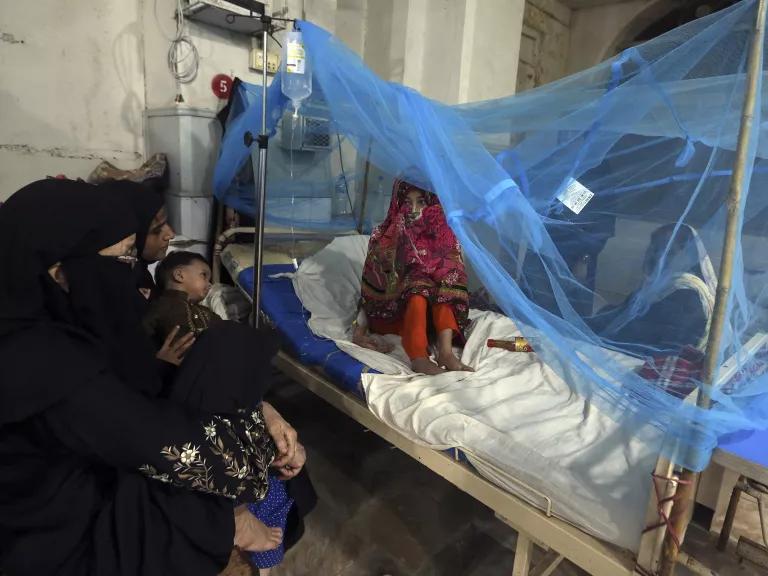 A girl sits on a hospital bed that is covered in blue netting.