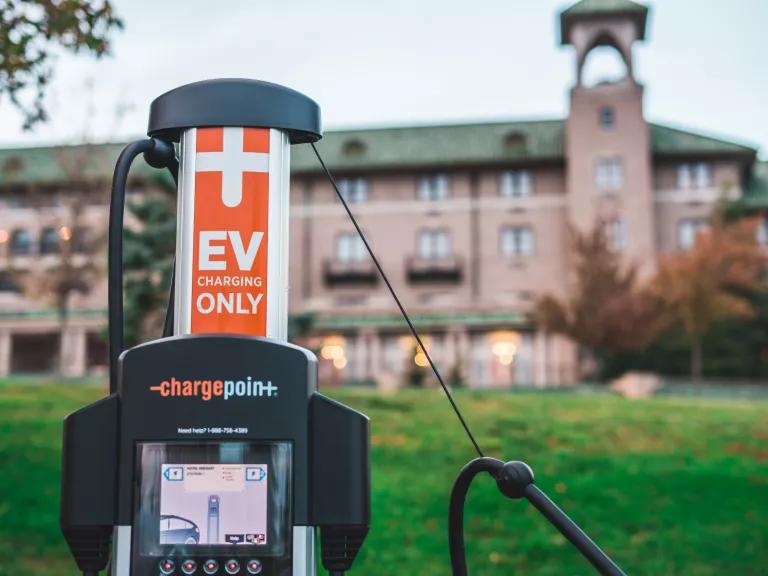 An electric vehicle charging station in a grassy area with a large building in the background