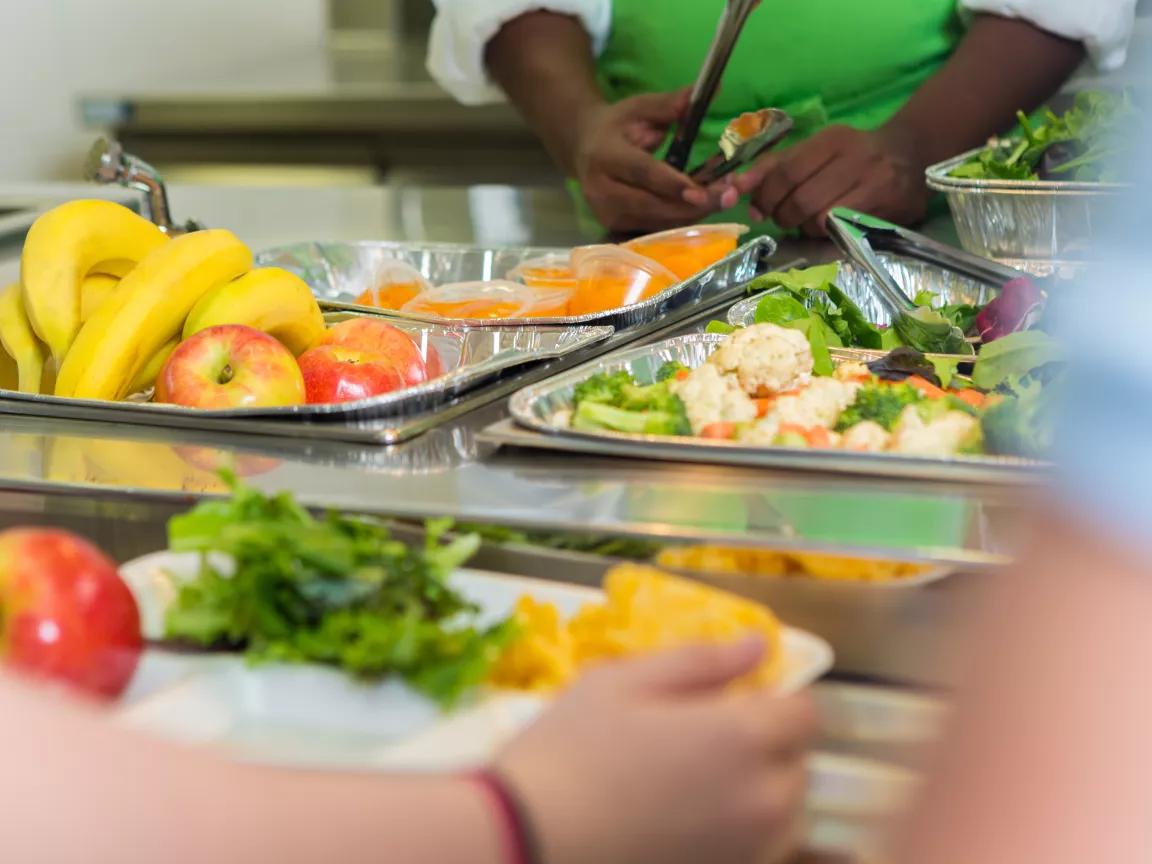 A table of trays of fresh foods with children's hands holding the trays