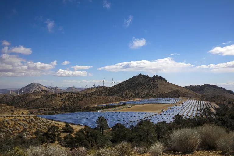 A solar array in a valley with wind turbines in the distance