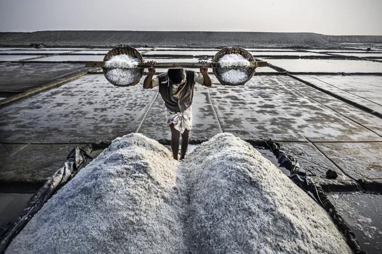 A man carries two large buckets of salt on his shoulders