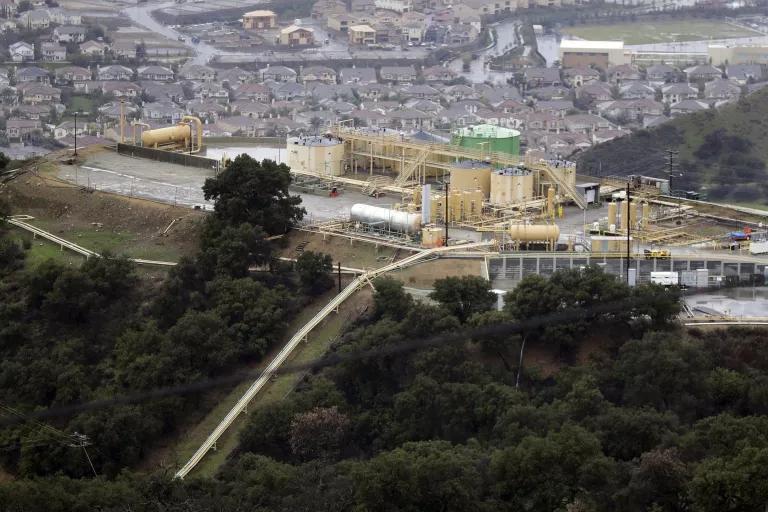 An aerial view of an industrial facility adjacent to a residential neighborhood on one side and forested area on the other