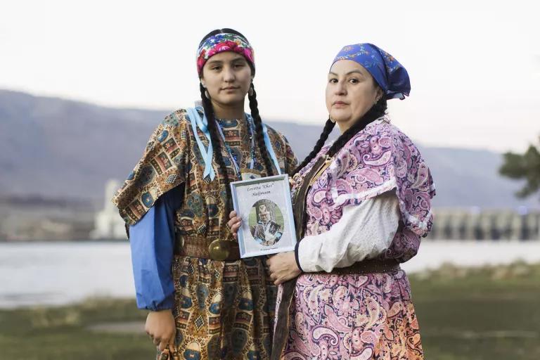 Two women stand in front of a river and hold a photograph between them