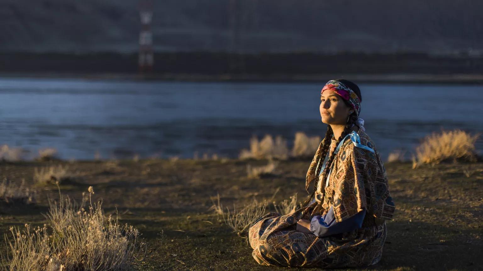 A woman sits on a riverbank