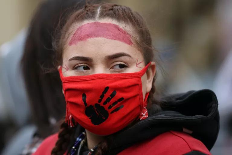 A woman wears a streak of red face paint on her forehead and a red face mask with a black palm print on it