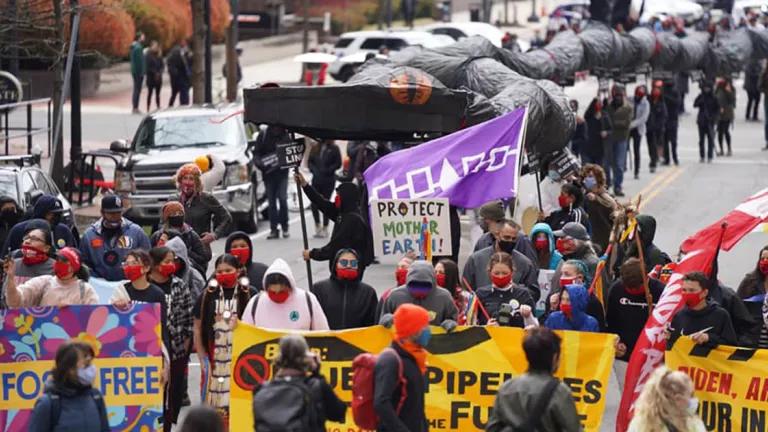 Protesters march on a city street wearing red face masks and carrying yellow banners