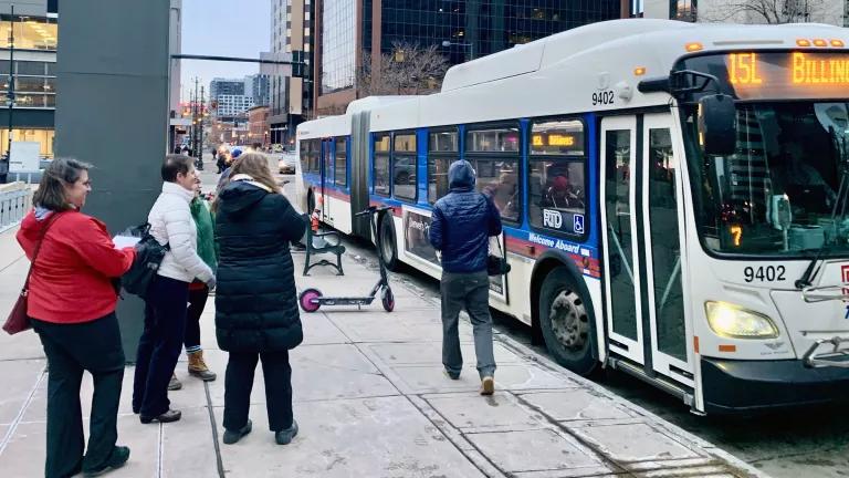 Several people wait at a bus stop as a bus pulls in