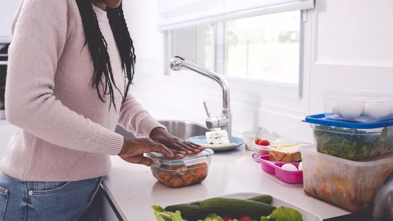 A woman stands at a kitchen counter closing the lid on a resealable containter full of vegetables