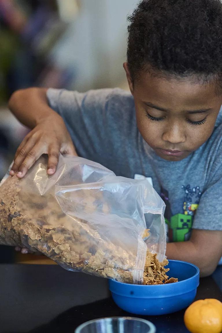 A child pouring cereal into a blue bowl