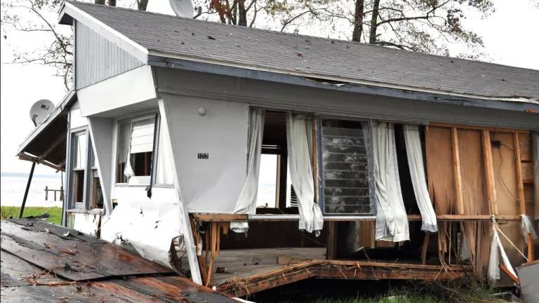 A severely damaged house with blown out windows and exposed plywood and framing