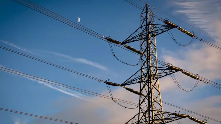 Power lines, as seen from below, with the moon rising in the sky behind them