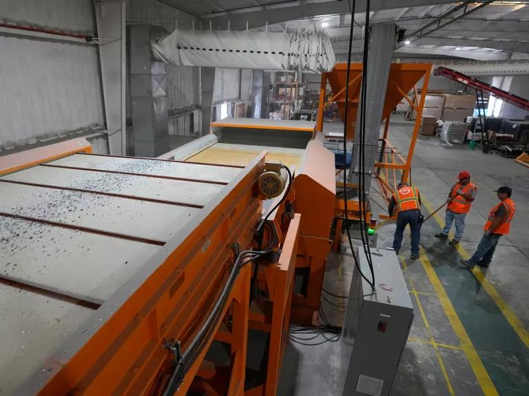 Small shards of a solar panel move on a large conveyor belt to be processed.