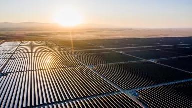 The sun shines across many acres of solar panels in a grassland plain.